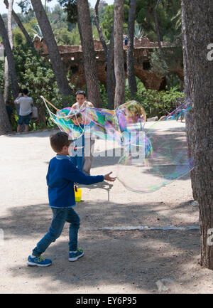 Kind, die jagen riesiger Seifenblasen erstellt von Straßenkünstler im Parc Güell, Barcelona Stockfoto