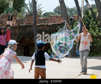 Kind, die jagen riesiger Seifenblasen erstellt von Straßenkünstler im Parc Güell, Barcelona Stockfoto