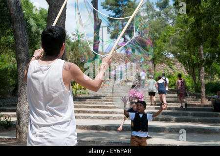 Kind, die jagen riesiger Seifenblasen erstellt von Straßenkünstler im Parc Güell, Barcelona Stockfoto