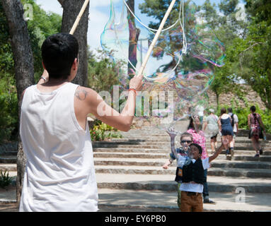 Kind, die jagen riesiger Seifenblasen erstellt von Straßenkünstler im Parc Güell, Barcelona Stockfoto