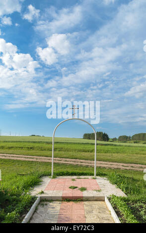 Weiße halbrunde Stahlbogen mit einem orthodoxen Kreuz auf dem Hintergrund der ländlichen Landschaft unter blauem Himmel mit der cloud Stockfoto