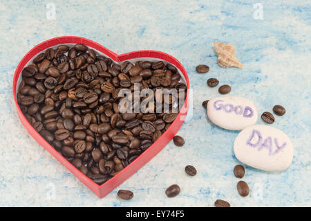 Herzförmige Box gefüllt mit gebratenen Kaffeebohnen auf blauem Hintergrund mit einem "guten Tag" Stockfoto