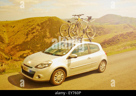 Ein fahrendes Auto mit zwei Fahrräder auf dem Dachgepäckträger Fahrt über den sonnigen Hügeln von Shropshire im England, UK. Stockfoto