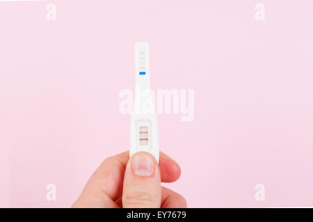 Männliche Hand mit positiven Schwangerschaftstest isoliert auf rosa Hintergrund. Glücklicher Vater. Stockfoto