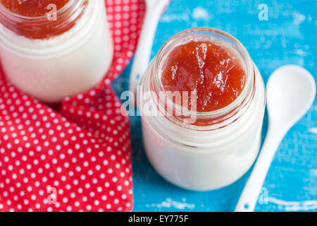 Hausgemachter Joghurt mit Apfelkonfitüre in zwei kleinen Gläsern auf a blaue Tabelle mit rotem Tuch, selektiven Fokus Stockfoto