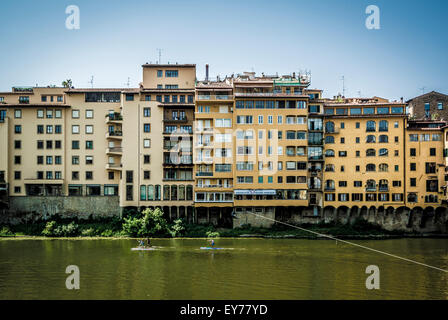Moderne Florentiner am Flussufer Gebäude mit zwei aufstehen Surfer paddeln auf dem Fluss Arno, Florenz, Italien. Stockfoto