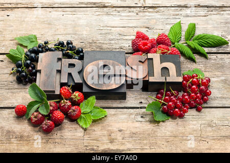 Word "Fresh" written with vintage letterpress printing blocks, surrounded by a variety of fresh berry fruits on wood background Stockfoto