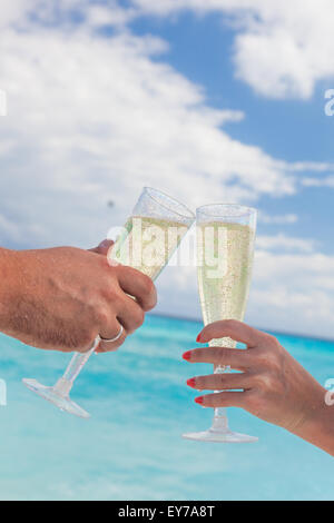 Klingende Gläser mit Champagner am Sandstrand und Meer Hintergrund, geringe Bautiefe Stockfoto