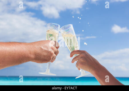 Klingende Gläser mit Champagner am Sandstrand und Meer Hintergrund, geringe Bautiefe Stockfoto