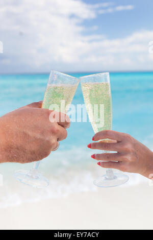 Klingende Gläser mit Champagner am Sandstrand und Meer Hintergrund, geringe Bautiefe Stockfoto