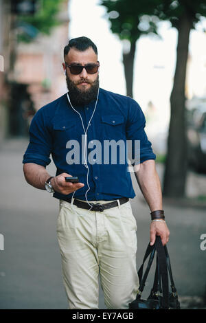 bärtiger Mann geht und hört Musik Stockfoto