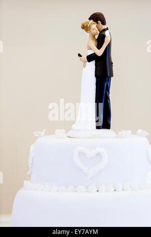 Eine Hochzeitstorte Topper mit Braut und Bräutigam Zeichen von SMS-Nachrichten auf Mobiltelefonen gleichzeitig umarmen einander. Eine ironische komische Szene Stockfoto