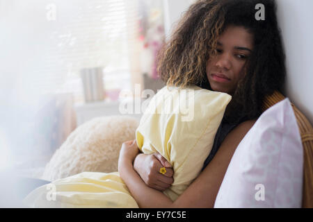 Teenager-Mädchen (14-15) sitzt auf Bett, Kissen umarmen Stockfoto