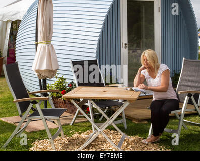 Caravan Klemmung Holzpod, draußen Picknick-Tische & Stühle Frau lesen Broschüre in Tatton Park, Cheshire, UK 23. Juli 2015. Eröffnungstag der RHS Flower Show. Stockfoto