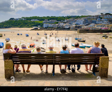 Cornwall im Sommer - in der Sommersaison sitzen Touristen auf einer Bank mit Blick auf den Hafen und den Strand in St Ives, England, Großbritannien Stockfoto
