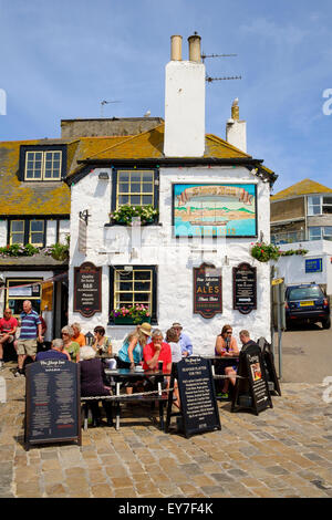 Touristen sitzen im Sommer außerhalb der alten Sloop Inn-Kneipe im Hafen von St. Ives, Cornwall, England, UK Stockfoto