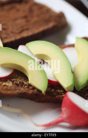 Avocado und Rettich Scheiben auf dunklem Brot mit Vollkorn-Senf bestreichen Stockfoto