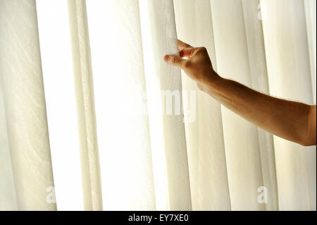 Die Hand eines Mannes ziehen ein Fenstervorhang für warme Tageslicht in den Raum zu betreten Stockfoto