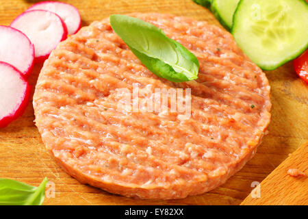 Rohe Burger Patty und geschnittene Gemüse auf Schneidebrett Stockfoto