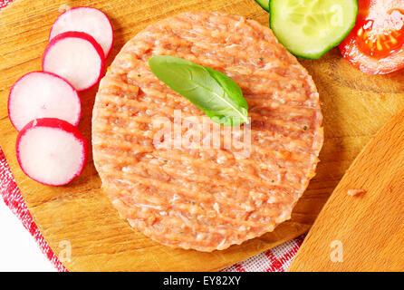 Rohe Burger Patty und geschnittene Gemüse auf Schneidebrett Stockfoto