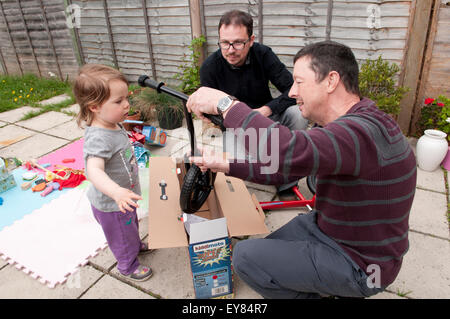 Kleines Mädchen öffnen ihr Geburtstagsgeschenk mit ihrem Großvater und Vater Stockfoto