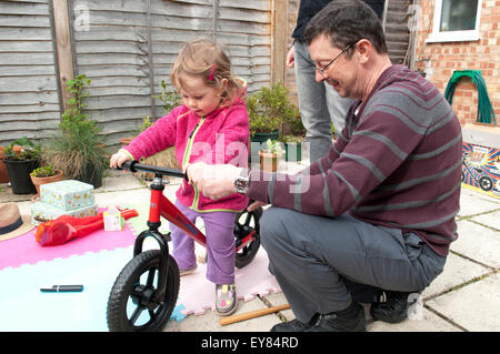 Kleines Mädchen sitzt auf ihr neues Laufrad zu präsentieren, von ihrem Großvater Stockfoto