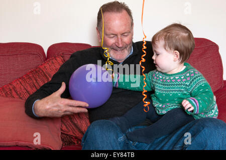 Babymädchen sitzen auf Schoß Großväter spielen mit einem Ballon Stockfoto
