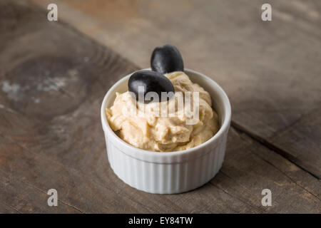 Cremige Hummus mit Oliven in einer kleinen Schüssel auf Holztisch Stockfoto