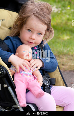 Glückliche kleine Mädchen im Kinderwagen kuscheln ihre Puppe Stockfoto