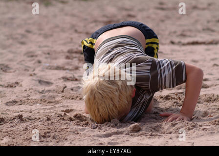 Blonde junge Graben ein tiefes Loch im Sand Stockfoto