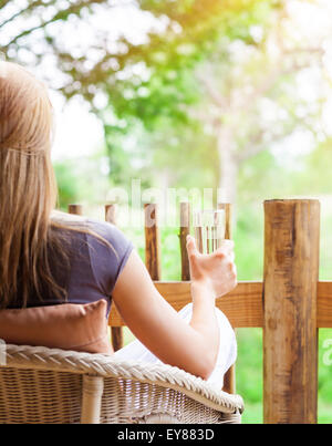 Ruhige Frau entspannen im Freien, Rückseite des weiblichen sitzen auf dem Stuhl auf der Terrasse, Trinkwasser und genießen schöne Natur Stockfoto