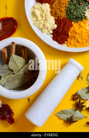 Buntes Kochen Gewürze und Kräuter auf eine Runde Platte mit Zimtstangen, Lorbeerblätter und Sternanis in Mörser und Stößel auf yello Stockfoto