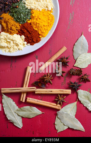 Buntes Kochen Gewürze und Kräuter auf Runde Platte mit Zimtstangen, Sternanis und Lorbeer auf Vintage rot Holztisch. Stockfoto