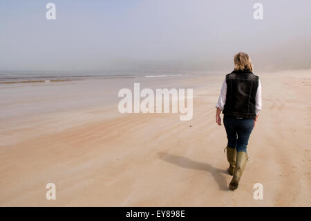 Rückansicht einer Frau allein zu Fuß am Sandstrand Stockfoto