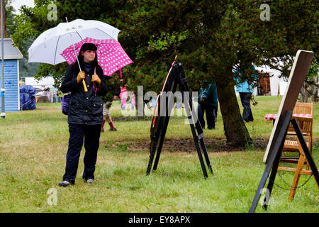 Malmesbury, Großbritannien. 24. Juli 2015. Atmosphäre im Charlton Park Festival WOMAD (World of Music, Arts and Dance) am 24.07.2015 in Charlton Park, Malmesbury.  Eine Frau steht im Regen mit zwei Schirme. Bildnachweis: Julie Edwards/Alamy Live-Nachrichten Stockfoto