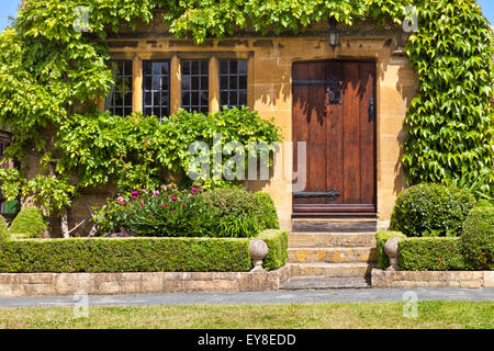 Eingang zum traditionellen englischen Honig golden braun stoned Hütte, mit Holztür, umgeben von grünen Reben, Mullion Windows, f Stockfoto
