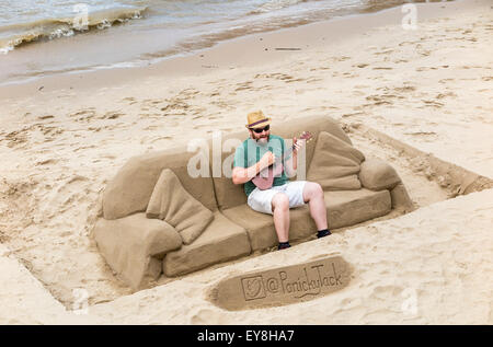 Sand Bildhauer Busker, Skulpturen für Tipps zu machen, als Straßenmusikant Gitarre auf einem Sand Sofa, Südufer des Embankment, London, UK Stockfoto