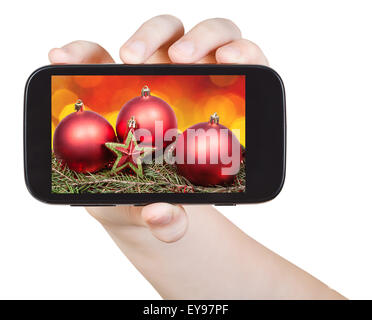 Hand hält Handphone mit Weihnachtsschmuck auf Bildschirm isoliert auf weißem Hintergrund Stockfoto