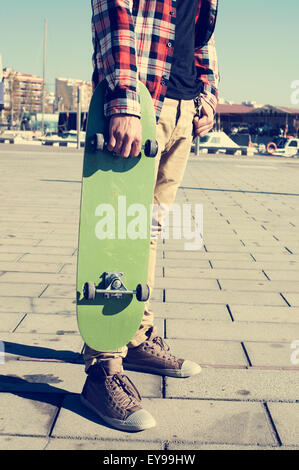 kaukasischen Jüngling trägt ein kariertes Hemd hält in seiner Hand eine grüne skateboard Stockfoto