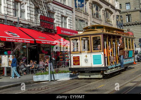 Ein Mann fährt mit einer Seilbahn, die draußen auf dem Trittbrett eine steile Steigung auf der Powell Street, San Francisco, Kalifornien, USA, hinunterfährt Stockfoto