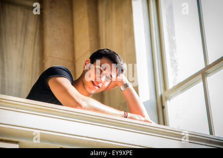 Portrait of Smiling attraktive jungen Mann stützte sich auf die Arme gegen polierten Marmor Treppe Geländer innen klassische Build Stockfoto