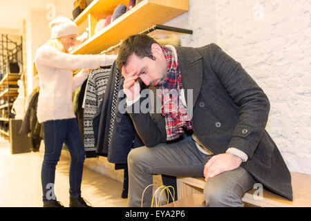 Blick auf eine junge legerer Mann warten, während seine Frau einkaufen ist Stockfoto