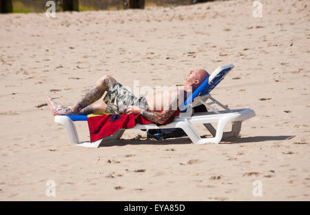 Bournemouth, Dorset, UK 25. Juli 2015. Mann mit Tattoos an Armen und Beinen, in kurzen Hosen, Sonnenbaden auf der Liege am Strand von Bournemouth im Juli Credit: Carolyn Jenkins/Alamy Live News Stockfoto