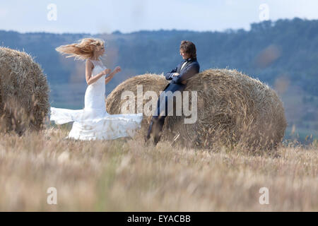 Verheiratete Paare, die Spaß auf einem Feld mit Heuballen. Sie macht eine schöne Wendung mit ihren Haaren und Kleidung im Wind während er adm Stockfoto