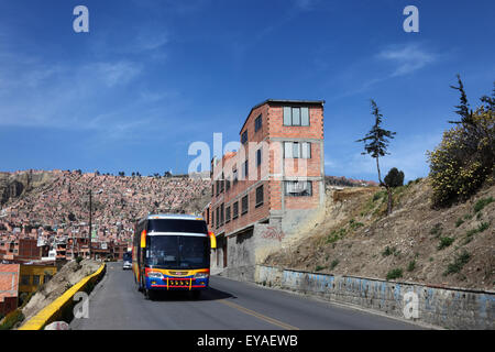Bus mit öffentlichen Verkehrsmitteln, der bergauf an einem Backsteingebäude im Stadtvorort La Paz, Bolivien, vorbeifährt Stockfoto