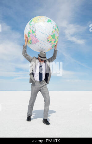 Geschäftsmann hält einen Globus der Erde über seinem Kopf stehend auf einsamen weißen Wüstenplaneten Stockfoto