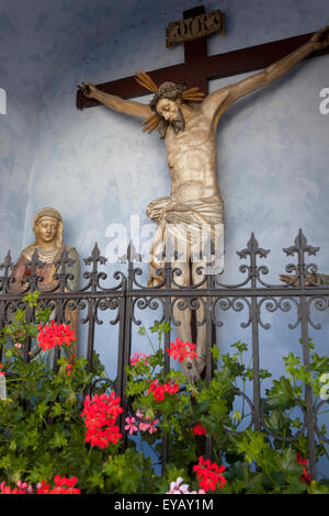Statue Jungfrau Maria und Jesus am Kreuz in der kleinen ländlichen Kapelle, Cesky Krumlov Tschechische Republik Pelargonium Blumen Stockfoto