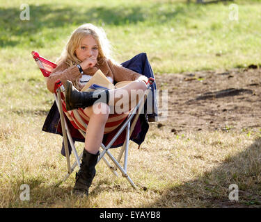 Malmesbury, Wiltshire, UK. 25. Juli 2015. Atmosphäre beim WOMAD (World of Music, Arts and Dance) Festival in Charlton Park auf 25.07.2015 bei Charlton Park, Malmesbury.  Ein junges Mädchen sitzt in der Abendsonne Harry Potter lesen. Bild von Julie Edwards/Alamy Live-Nachrichten Stockfoto