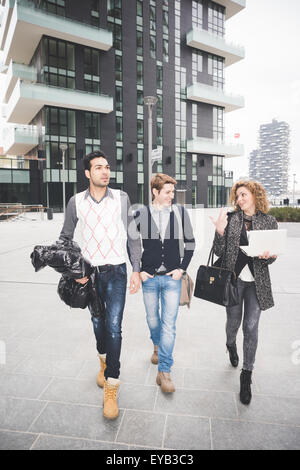 Gemischtrassig zeitgenössischen Geschäftsleute gehen und arbeiten durch die Stadt mit technischen Geräten wie Laptop-Finance, Stockfoto