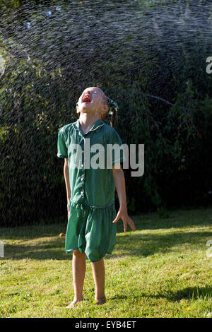 Mädchen im grünen Kleid spielen unter einem Wasser Sprinkler. Stockfoto
